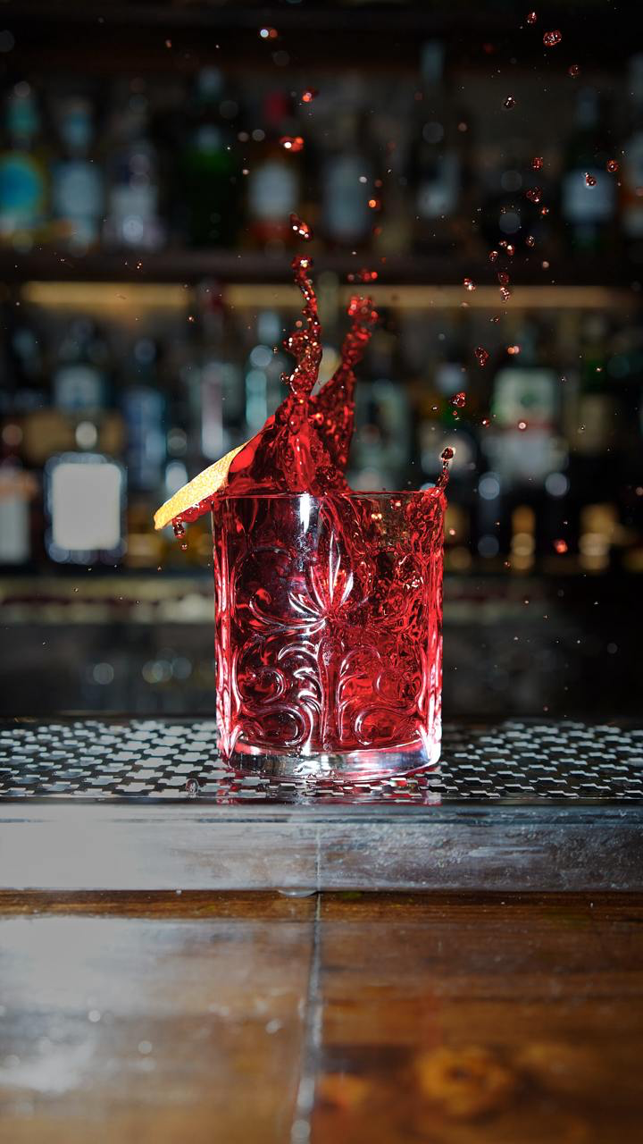 Cocktail rosso con una scorza di agrume e uno spruzzo sopra il bicchiere